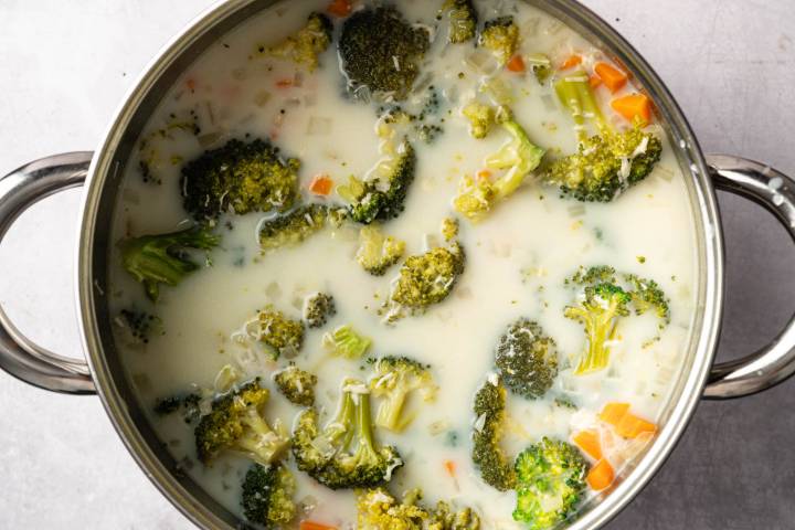 A pot of creamy broccoli soup with visible chunks of broccoli and diced carrots, creating a warm and comforting appearance on a light background.